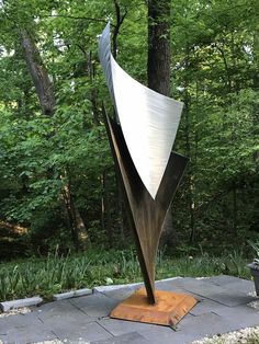 a large metal sculpture sitting on top of a cement slab next to a forest filled with trees