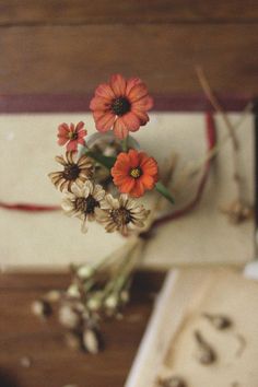 three orange flowers are in a vase on a table next to a book and other items