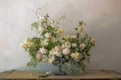 a vase filled with lots of flowers on top of a wooden table next to a wall