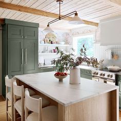 a kitchen with green cabinets and an island in front of the stove top is filled with fruit