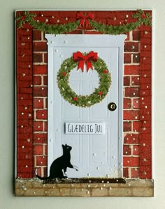 a cat sitting in front of a white door with a wreath on it's side