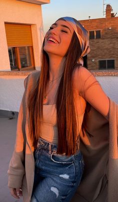 a young woman sitting on top of a roof next to a building with her hands behind her head