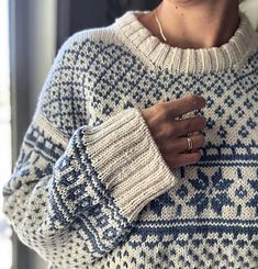 a woman wearing a blue and white sweater is holding her hand on her chest while looking at the camera