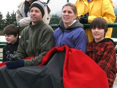 a group of people sitting next to each other on top of a bench in front of a fence