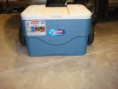 a blue cooler sitting on the ground in front of a car with a cell phone attached to it