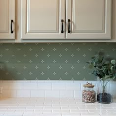 a kitchen with white cabinets and green backsplash wallpaper on the counter top