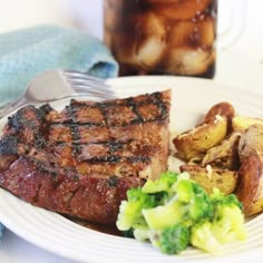 steak, potatoes and broccoli on a white plate with a beverage in the background