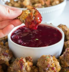 a person dipping something into a small white bowl filled with cranberry sauce and meatballs