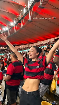 a woman in a red and black shirt at a soccer game with her arms up