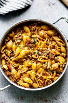 a pot filled with pasta and meat on top of a table next to utensils