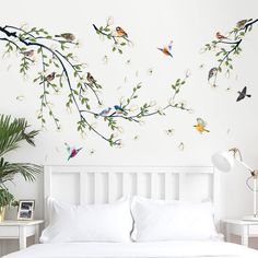 a white bed sitting next to a wall with birds flying on it's branches