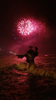 two people standing in the water with fireworks behind them