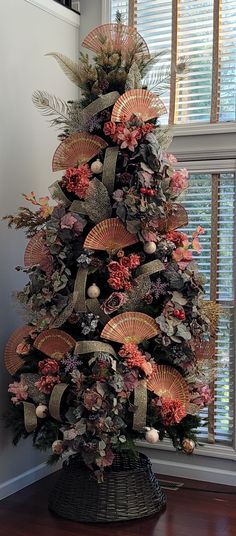 a decorated christmas tree in front of a window with flowers and fan decorations on it