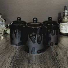 three black canisters sitting on top of a wooden table next to bottles and glasses