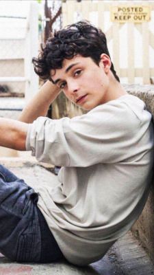 a young man sitting on the ground with his hand on his head and looking at the camera