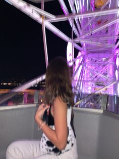 a woman sitting on top of a white bench next to a ferris wheel at night