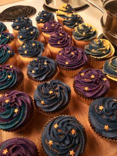 cupcakes with blue and purple frosting are arranged on a wooden board next to a stove