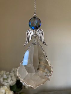 an angel ornament hanging from a chain on a table with flowers in the background