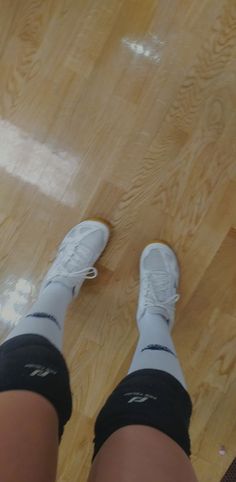 a person standing on a hard wood floor with their legs crossed and white sneakers on