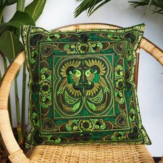 a green and yellow pillow sitting on top of a wicker chair next to a potted plant