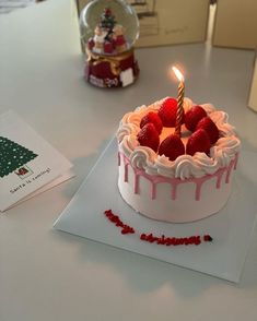 a birthday cake with white frosting and strawberries on top, next to a christmas tree