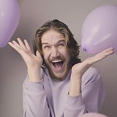 a man with long hair and beard holding balloons in front of his face as he laughs