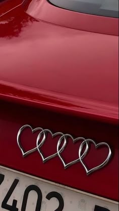 three hearts are attached to the hood of a red sports car with chrome lettering on it