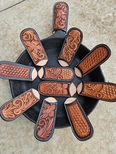 six leather knives are arranged in a circle on a black plate with brown and tan patterns