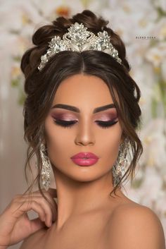 a woman wearing a tiara and makeup looks down at her face with flowers in the background