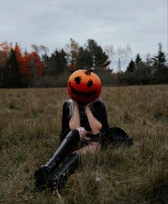 a woman sitting in the grass with an orange ball on her head and trees behind her