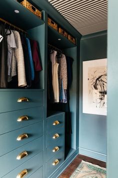 a closet with blue drawers and gold pulls on the doors, open to reveal an assortment of clothes