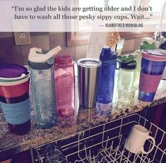 there are many cups on the counter in front of the dishwasher, and one is empty