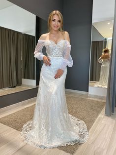 a woman standing in front of a mirror wearing a white wedding dress with long sleeves