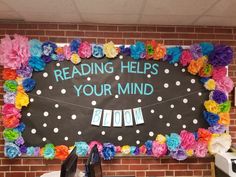 a bulletin board that reads reading helps your mind with flowers and paper pom poms