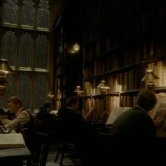 people sitting at tables in a library with bookshelves and lamps on the walls