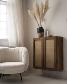 a white chair sitting in front of a wooden cabinet next to a vase with flowers