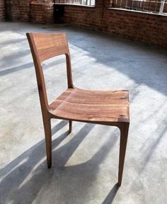 a wooden chair sitting on top of a cement floor next to a brick building with windows