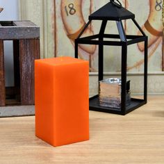 an orange candle sitting on top of a wooden table next to a small black lantern