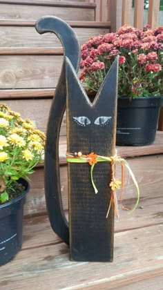 a black cat statue sitting on top of a wooden bench next to potted plants