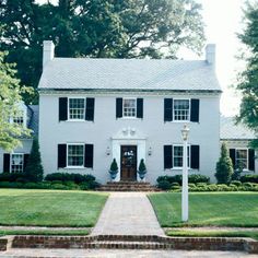 a large white house with black shutters on the front door and steps leading up to it