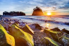 the sun is setting over some rocks on the beach