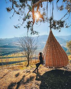 a woman sitting on a hammock hanging from a tree in the sun with mountains behind her