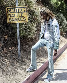 a man with dreadlocks standing next to a caution rattle - snakes road sign