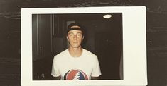 an old photo of a man in a white shirt and black cap with a lightning logo on it