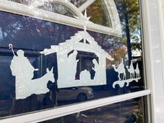 the window is decorated with white silhouettes of people and a christmas nativity scene