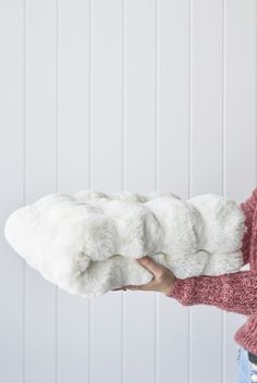 a woman is holding a white blanket in front of her face and she's wearing a pink sweater