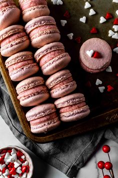 pink macaroons with white and red sprinkles on a baking sheet