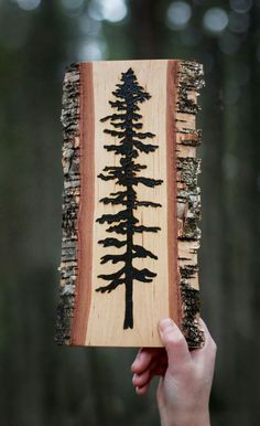 a person holding up a piece of wood with trees on it