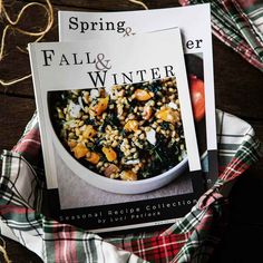 two cookbooks sitting on top of a table next to some vegetables and fruit in a bowl