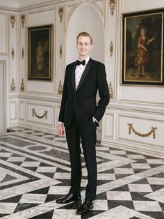 a young man in a tuxedo poses for a photo at an art gallery